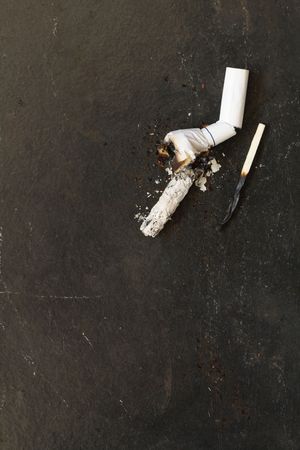 Cigarette butt with ashes and burnt match lying on dark backgroundの写真素材