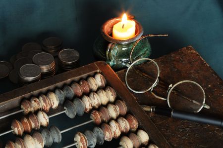 Vintage still life with candle and old things: counting frame, coins, book, spectaclesの写真素材