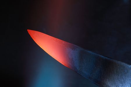 Abstract dark background with closeup of red-hot knife in flameの写真素材
