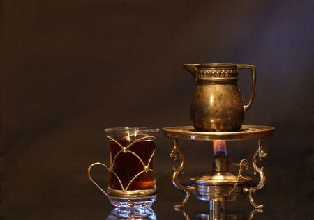 Cup of tea near ancient brass jug standing on vintage table spirit lamp with flameの写真素材