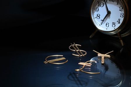 World currency signs made from brass wire near clock on dark background with copy spaceの写真素材