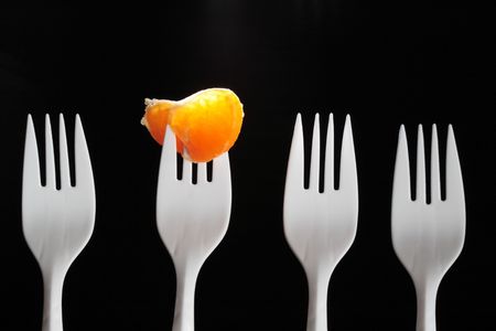 Four white plastic forks on dark. One fork with tangerine segmentの写真素材
