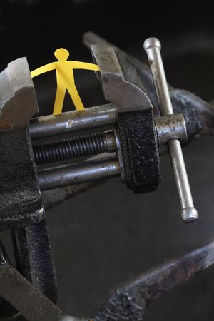 Small yellow paper man under pressure with old vise grip on abstract industry backgroundの写真素材