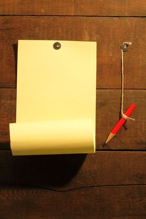 Yellow paper and red pencil hanging on wooden background with thumbtacksの写真素材