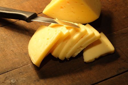 Sliced cheese and knife lying on wooden backgroundの写真素材
