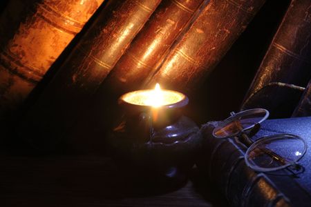 Closeup of candle with burning flame on vintage books background and old spectaclesの写真素材