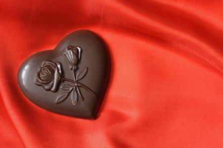 Closeup of chocolate heart lying on red silk textile with copy spaceの写真素材