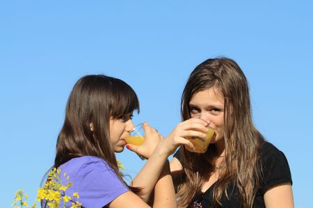 Two beauty teenage girls drinking orange juice against the blue skyの写真素材