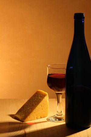 Bottle of red wine, wineglass and piece of cheese on wooden tableの写真素材