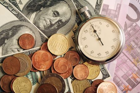 Closeup of stopwatch lying on background made from bank notes and coinsの写真素材