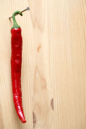 Red hot chili pepper hanging with nail on wooden backgroundの写真素材