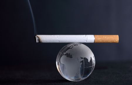 Conceptual balance: smoking cigarette lying on glass globe on dark backgroundの写真素材