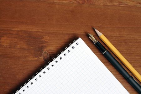 Closeup of blank spiral notebook near pen and pencil on wooden table