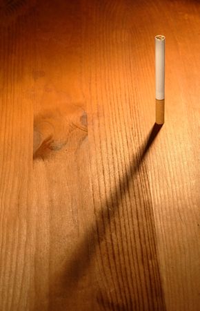 One cigarette standing on wooden background with long shadowの写真素材