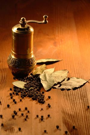 Vintage still life with brass pepper mill standing on wooden table near bay leaves and peppercornsの写真素材