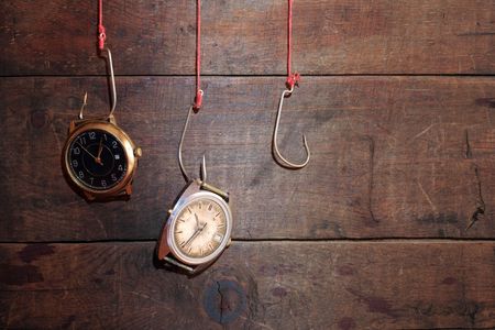 Two old watches hanging on fish hooks on wooden backgroundの写真素材