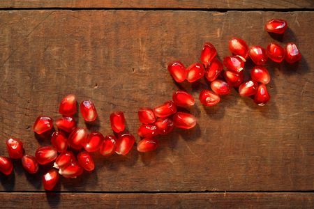 Lot of red pomegranate seeds lying in a row on dark wooden boardの写真素材