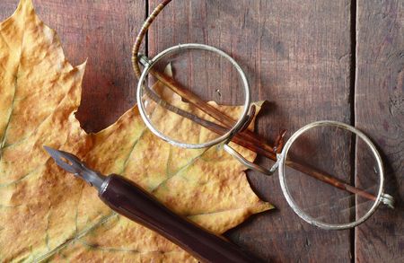 Vintage still life with dry maple leaf, ink pen and old spectacles lying on wooden backgroundの写真素材