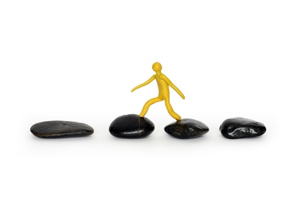 Yellow plasticine man walking on black stones. Isolated on white の写真素材