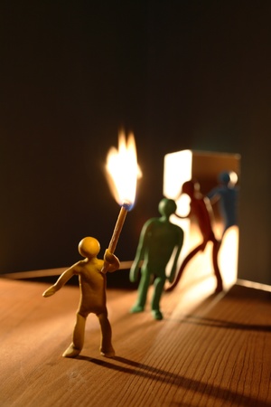 Few plasticine men with lighting match entering to dark room. Conceptual composition with open door made from paperの写真素材