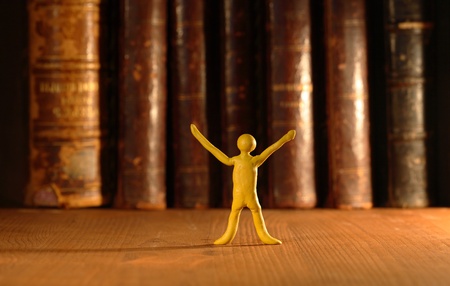 Small yellow plasticine man standing on background with old books in a rowの写真素材