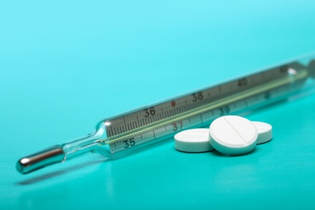 Stack of pills near clinical thermometer on green background