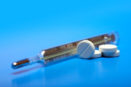 Stack of pills near clinical thermometer on blue background