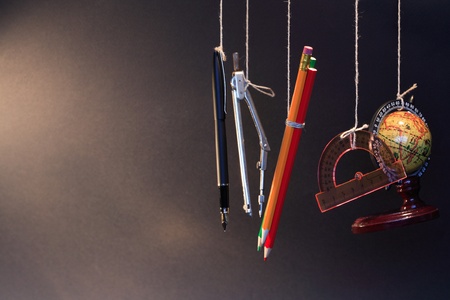 Color pencils, fountain pen and other objects hanging with ropes on dark backgroundの写真素材