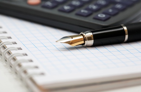 Closeup of black fountain pen lying on spiral notebook near calculatorの写真素材