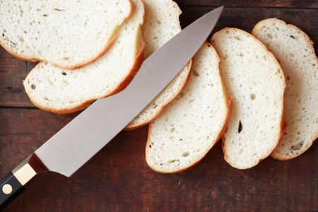 Sliced white bread and kitchen knife on wooden surface