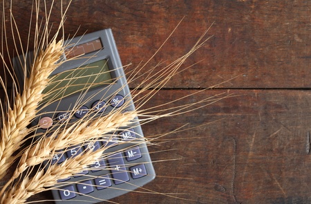 Ears of wheat and calculator lying on wooden surface with copy spaceの写真素材