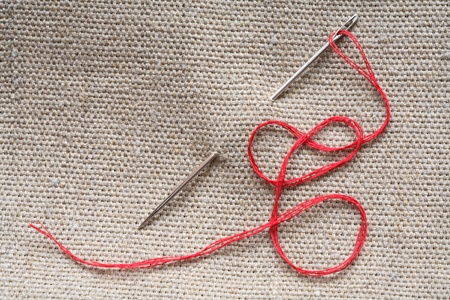 Needle with red thread attached to canvas surface