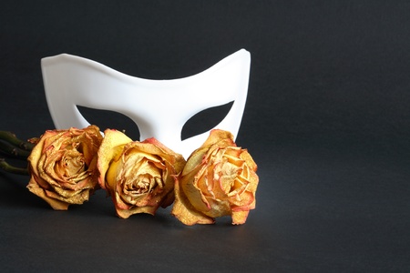 White venetian mask and dry yellow roses on black backgroundの写真素材