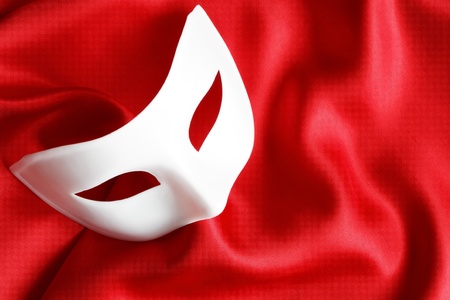 White venetian mask lying on red silk backgroundの写真素材