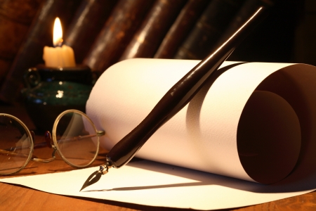 Scroll and old spectacles and ink pen near lighting candle on wooden surfaceの写真素材