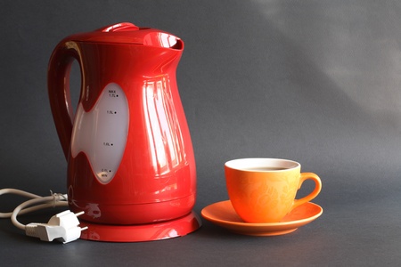 Nice modern red electric kettle near cup of tea on dark backgroundの写真素材