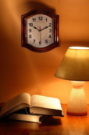Still life with luminous desk lamp near old books and clockの写真素材