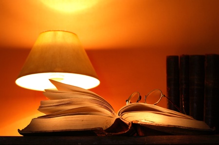 Luminous desk lamp near ancient books on ginger background with beam of lightの写真素材