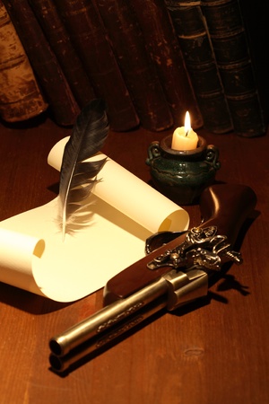 Ancient pistol near scroll and quill on wooden surface with lighting candleの写真素材
