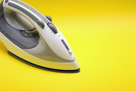 Closeup of gray modern electric iron on yellow backgroundの写真素材