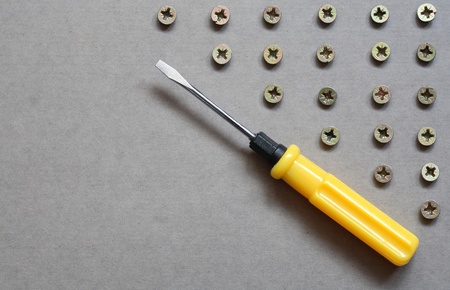 Industrial concept. Yellow screwdriver near lot of screws on gray surface with copy spaceの写真素材