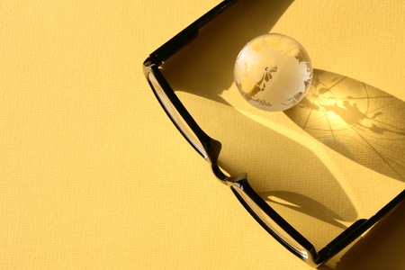 Business concept. Glass globe near modern black spectacles on yellow surface