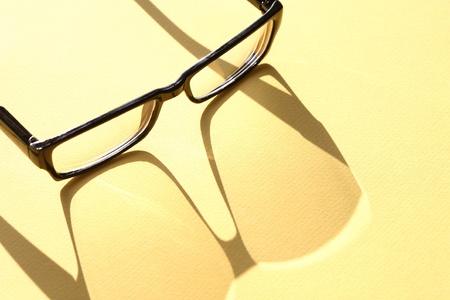 Closeup of spectacles with long shadow on yellow surfaceの写真素材