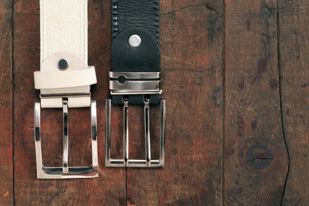 White and black leather belts hanging on old wooden background