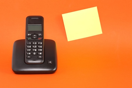 Modern black wireless telephone near blank yellow adhesive note on red backgroundの写真素材