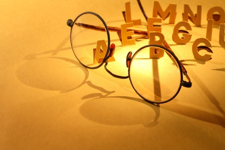 Reading concept. Old spectacles on yellow paper surface with cutting lettersの写真素材