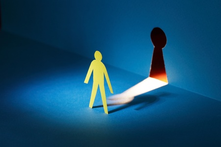 Spying concept. Yellow paper man standing against glowing keyholeの写真素材