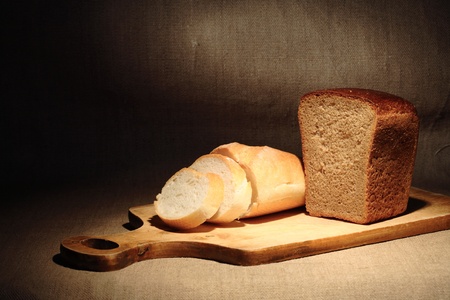 Still life with sliced bread on cutting board under beam of light