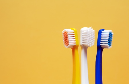 Three multicolored toothbrushes on yellow background with free space for text