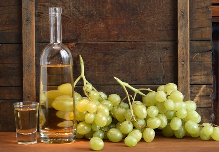 Glass full of grape Italian vodka grappa near bottle and bunch of grapes on old wooden backgroundの写真素材